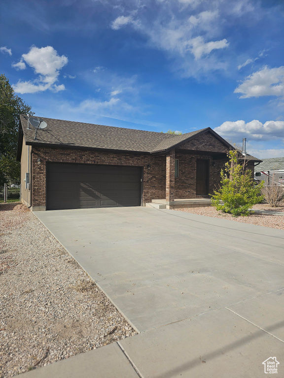 Ranch-style house with driveway, a garage, a shingled roof, and brick siding