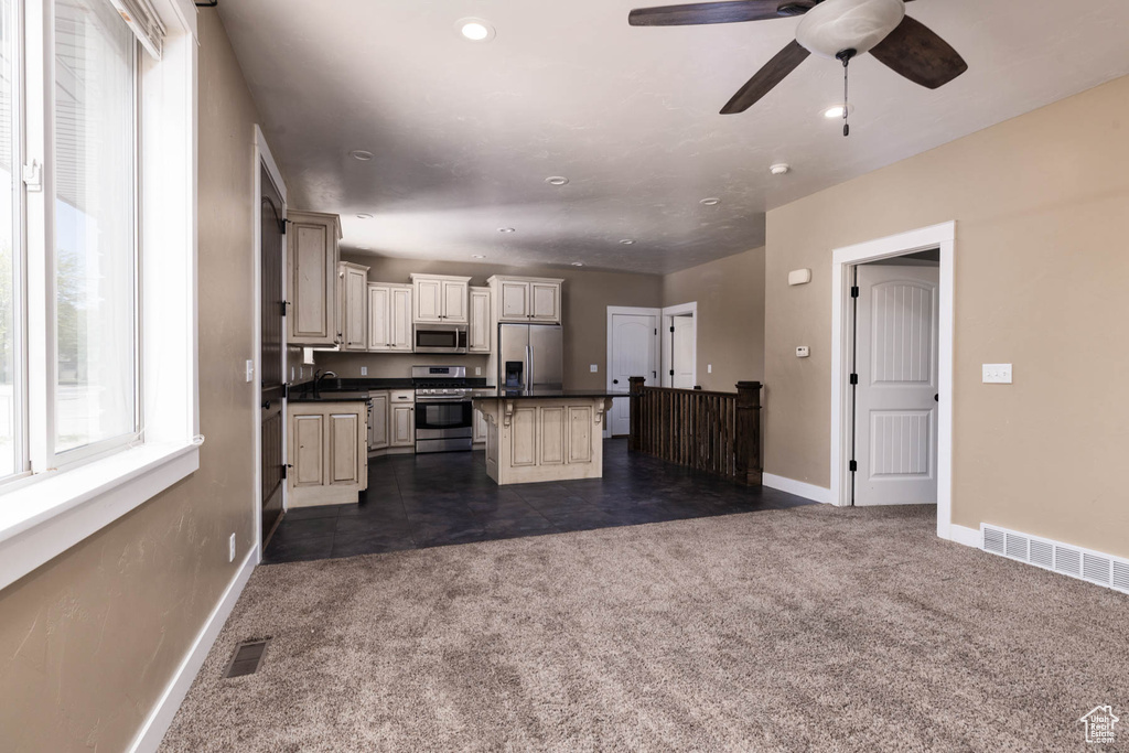 Kitchen with stainless steel appliances, cream cabinets, dark countertops, dark colored carpet, and baseboards
