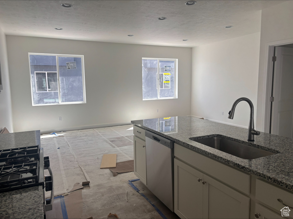 Kitchen featuring stainless steel dishwasher, a sink, stone countertops, and recessed lighting
