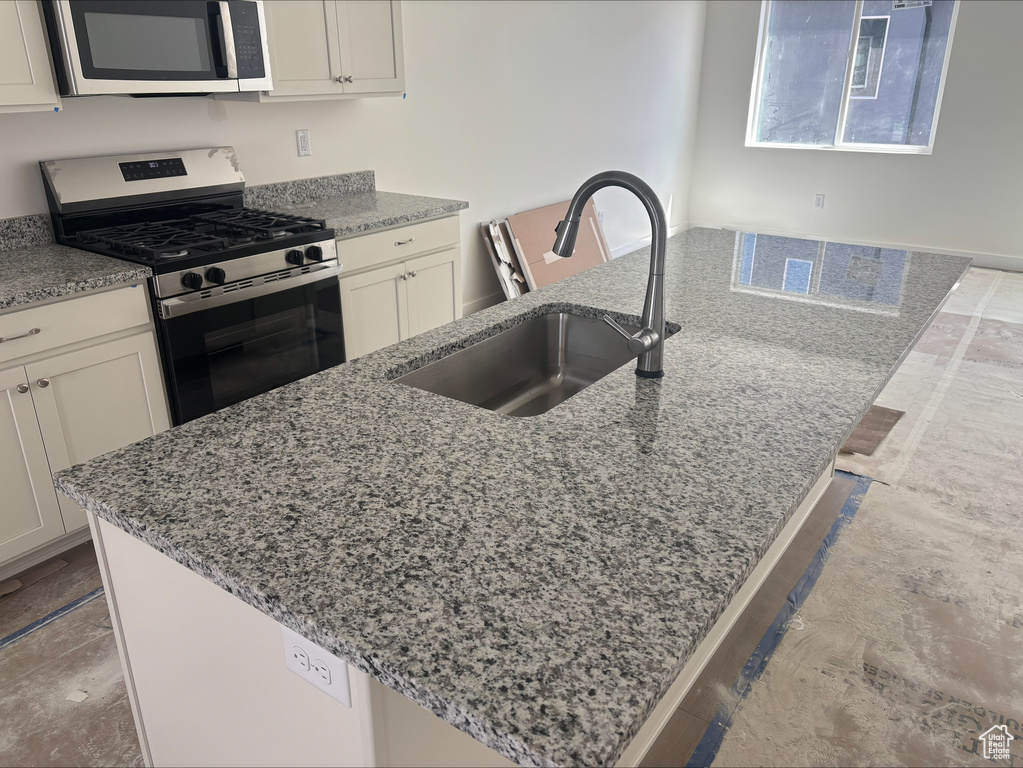 Kitchen with a sink, appliances with stainless steel finishes, and light stone countertops