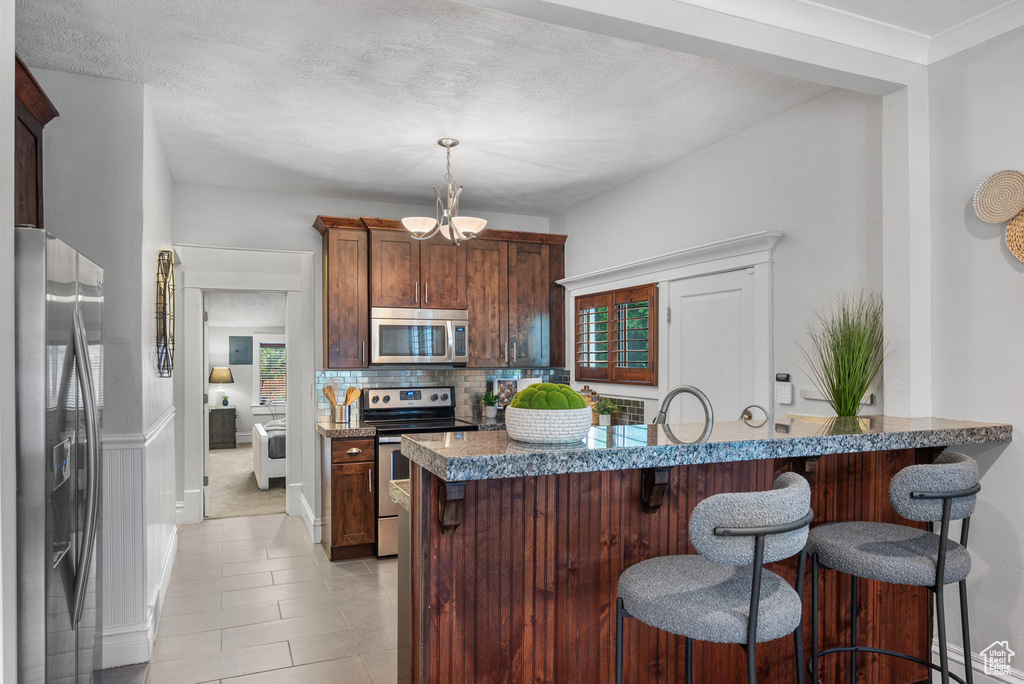 Kitchen featuring stainless steel appliances, a kitchen bar, a chandelier, decorative backsplash, and hanging light fixtures