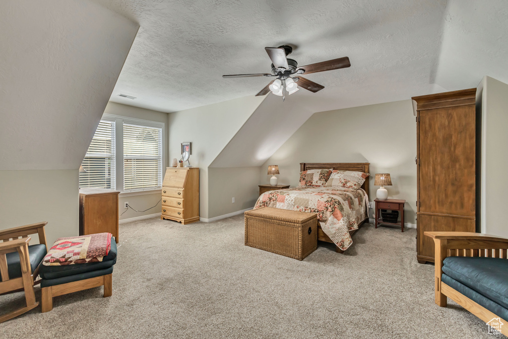 Bedroom featuring lofted ceiling, a textured ceiling, light colored carpet, baseboards, and a ceiling fan