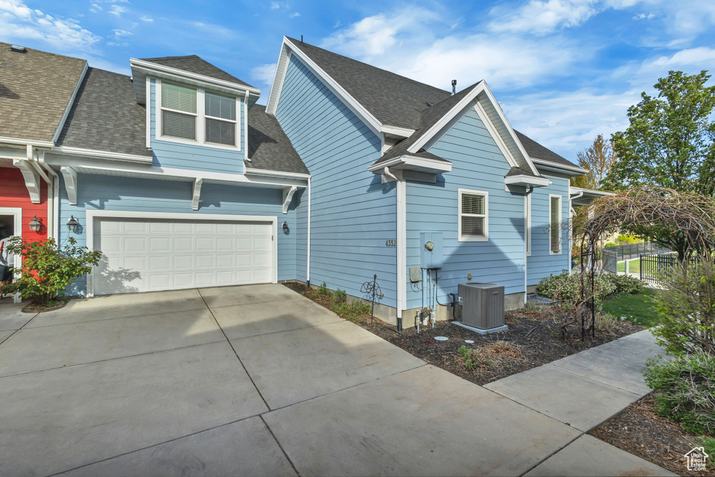 View of property exterior featuring driveway, roof with shingles, cooling unit, and an attached garage
