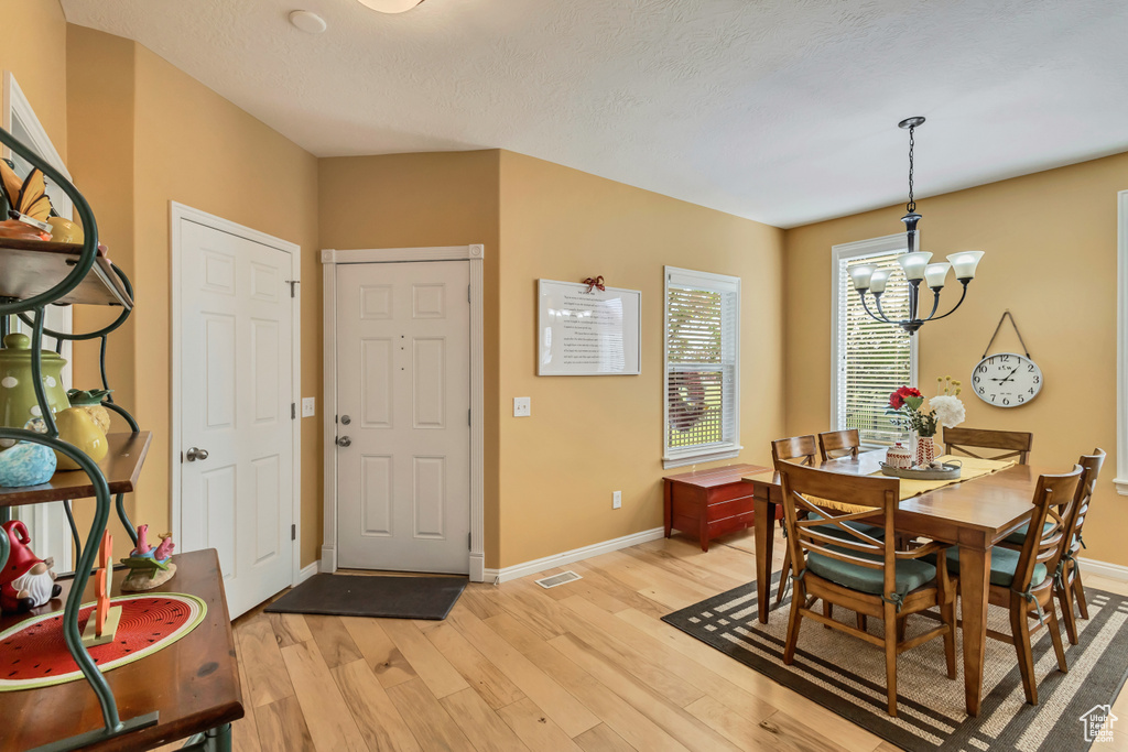 Dining space featuring a textured ceiling, visible vents, baseboards, an inviting chandelier, and light wood finished floors