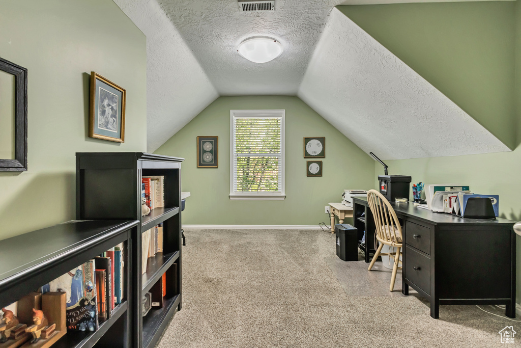 Carpeted office space with a textured ceiling, visible vents, lofted ceiling, and baseboards