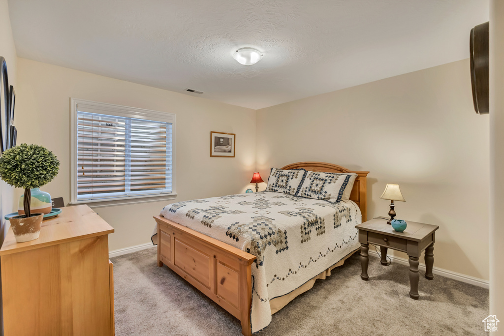 Bedroom featuring baseboards, visible vents, a textured ceiling, and light colored carpet