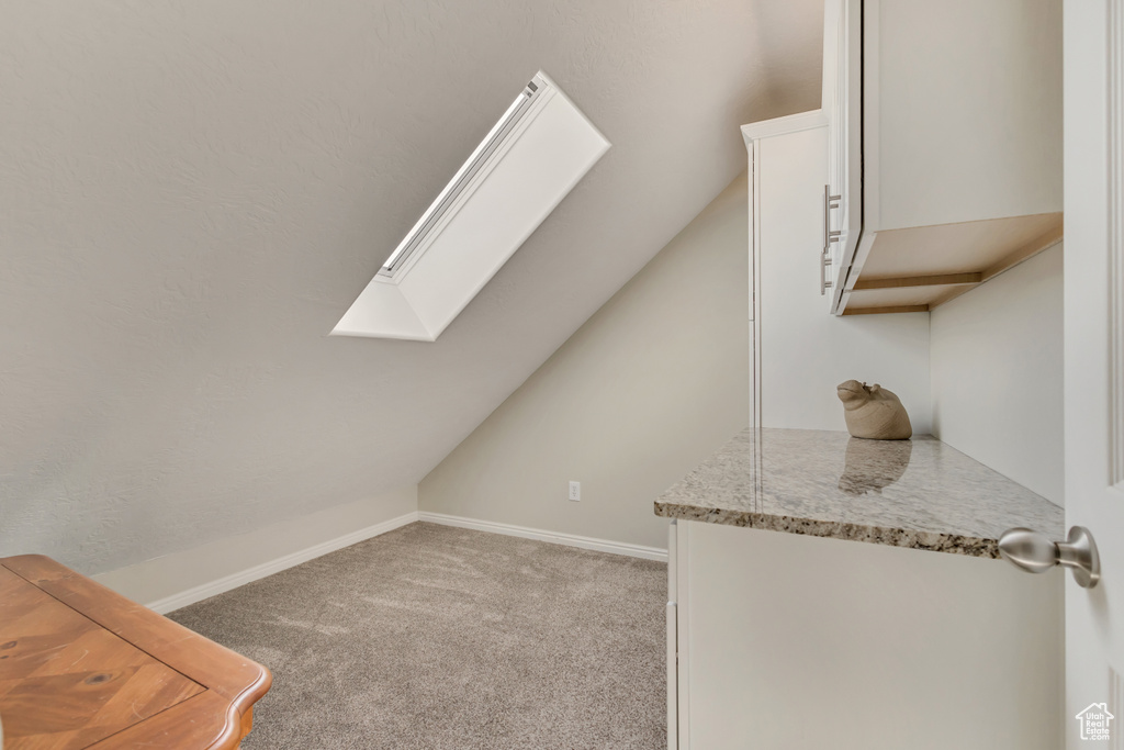 Additional living space featuring light colored carpet, baseboards, and lofted ceiling with skylight