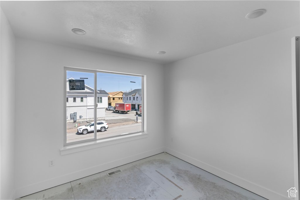 Empty room with concrete floors, visible vents, and baseboards