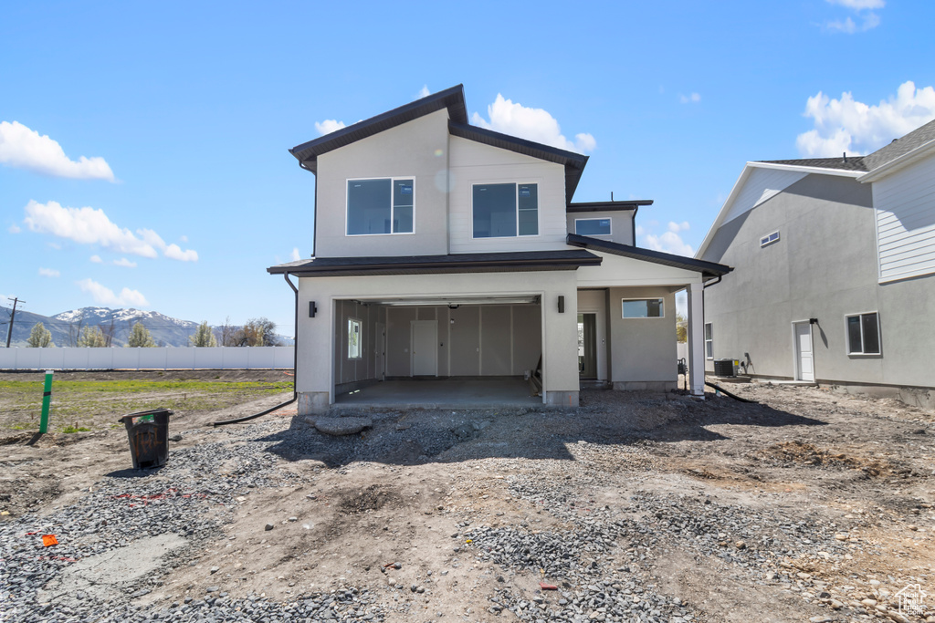 View of front of home with cooling unit, dirt driveway, a mountain view, an attached garage, and fence