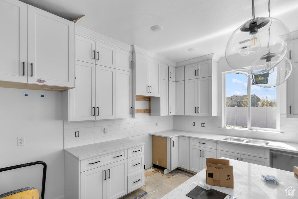 Kitchen with light stone counters, white cabinetry, tasteful backsplash, a sink, and hanging light fixtures