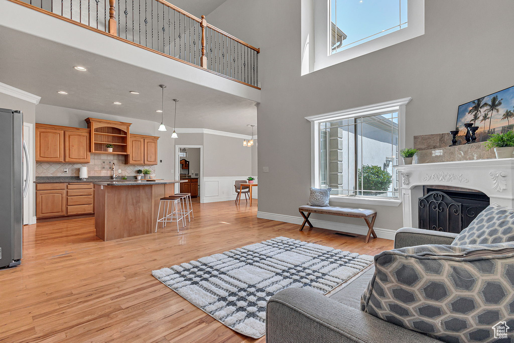 Living area featuring light wood-style floors, a fireplace, a high ceiling, ornamental molding, and baseboards