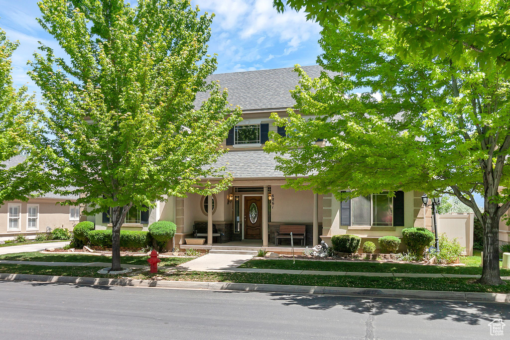 Obstructed view of property with stucco siding, a porch, and roof with shingles