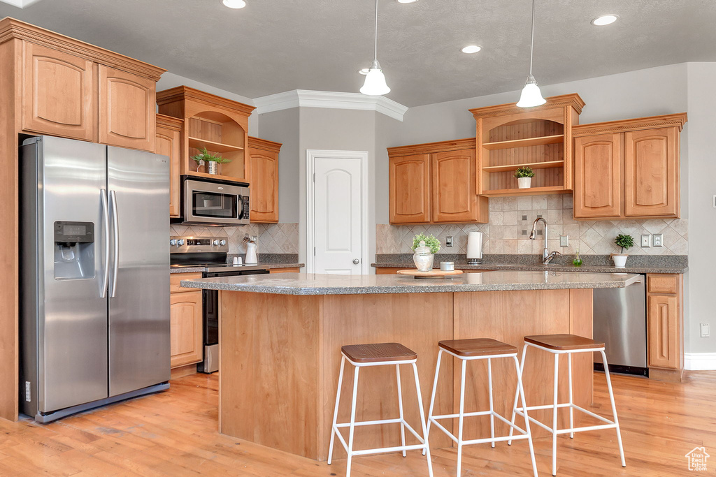 Kitchen with open shelves, stainless steel appliances, light wood-type flooring, a center island, and a kitchen bar