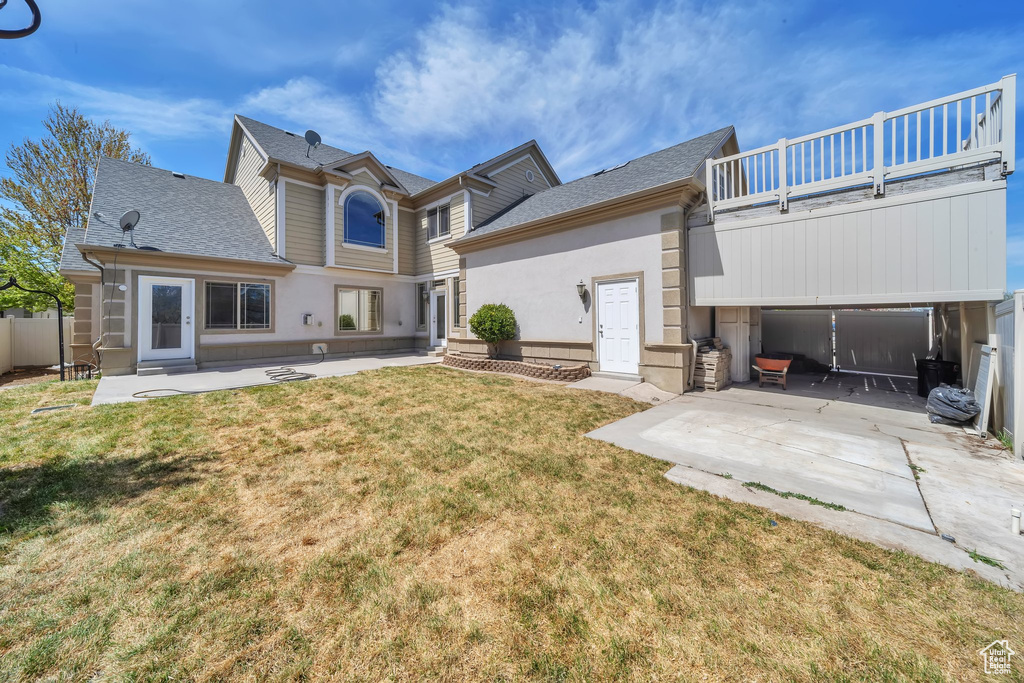 Rear view of property with a patio, roof with shingles, a yard, and a balcony