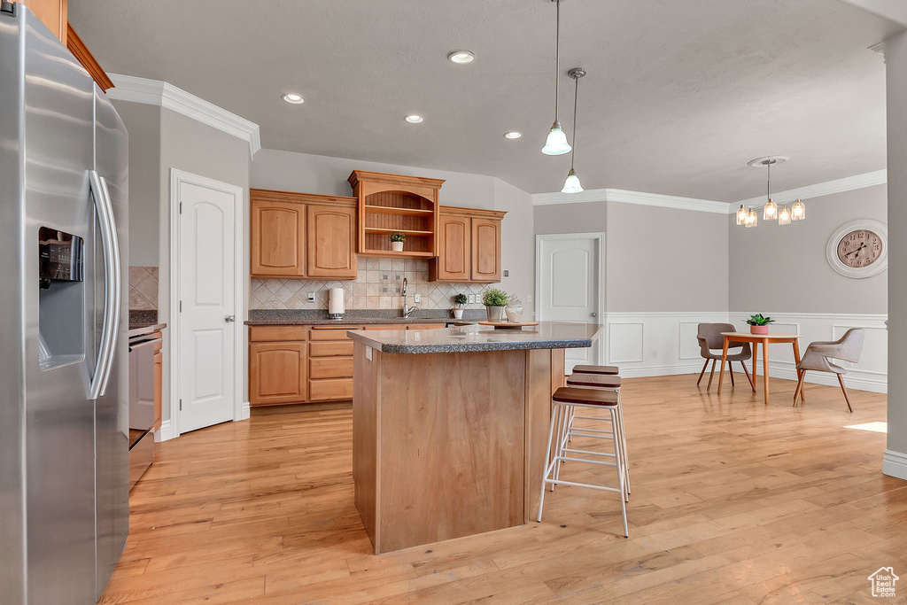 Kitchen with stainless steel fridge, a kitchen island, crown molding, open shelves, and a breakfast bar