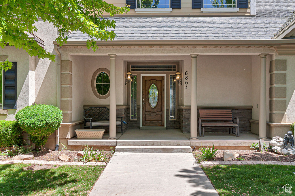 View of exterior entry with covered porch, stucco siding, roof with shingles, and stone siding
