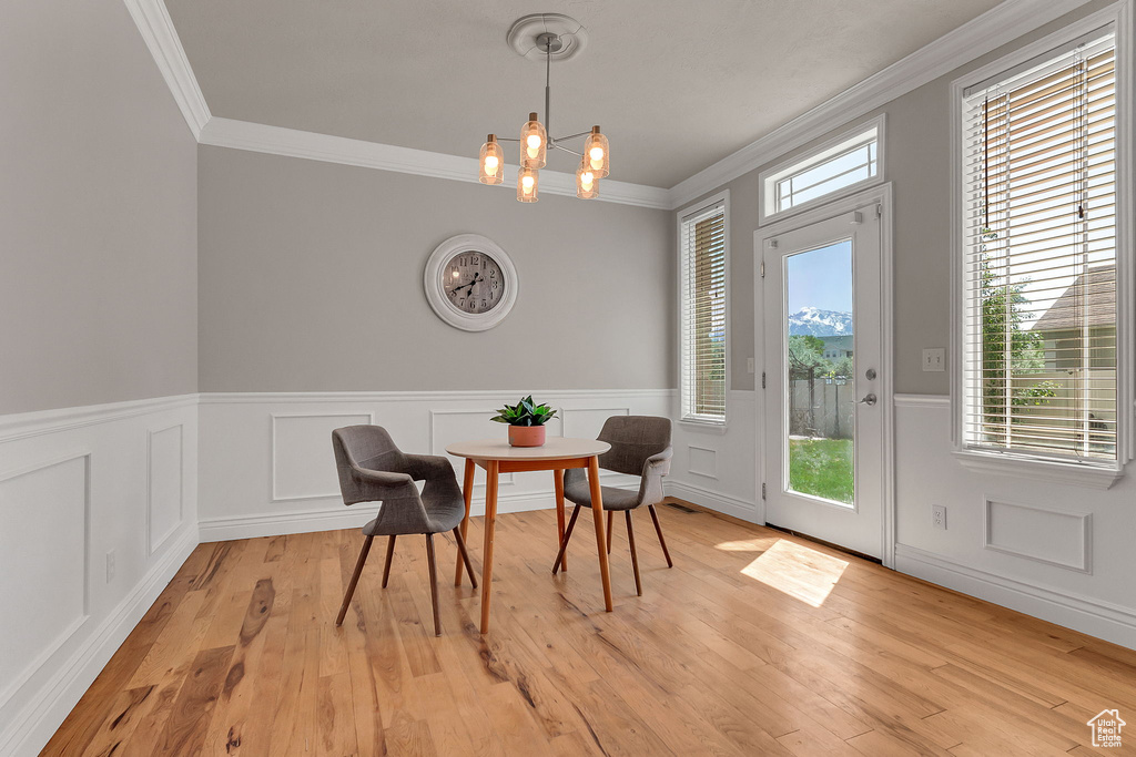 Dining space featuring crown molding, a wainscoted wall, a chandelier, and light wood finished floors