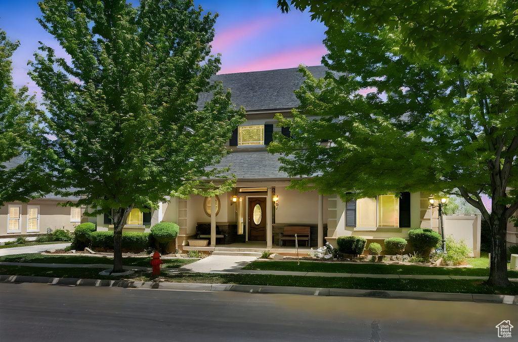 View of property hidden behind natural elements with stucco siding and a porch