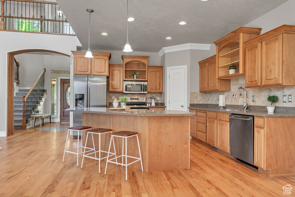 Kitchen featuring open shelves, stainless steel appliances, a sink, a kitchen island, and a breakfast bar