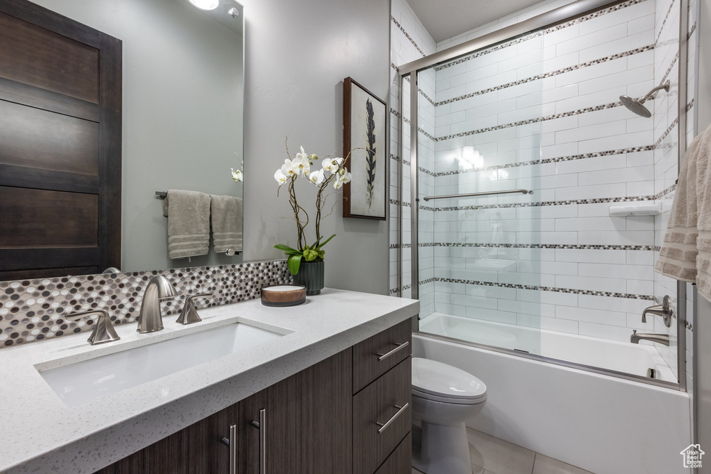 Full bathroom with tile patterned flooring, decorative backsplash, combined bath / shower with glass door, toilet, and vanity