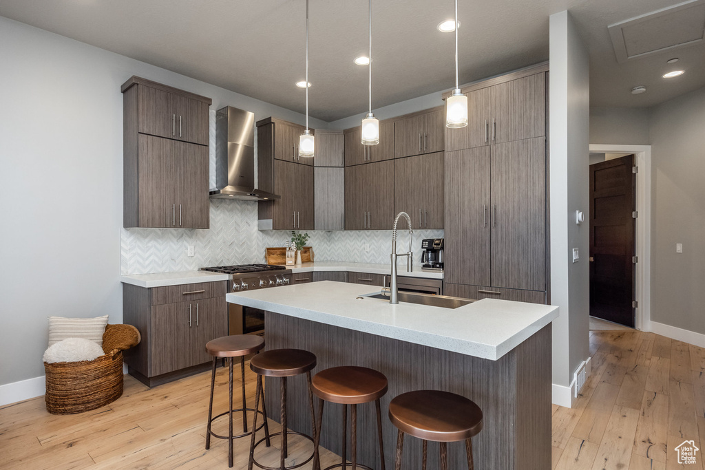Kitchen with high end range, a sink, wall chimney range hood, and light countertops