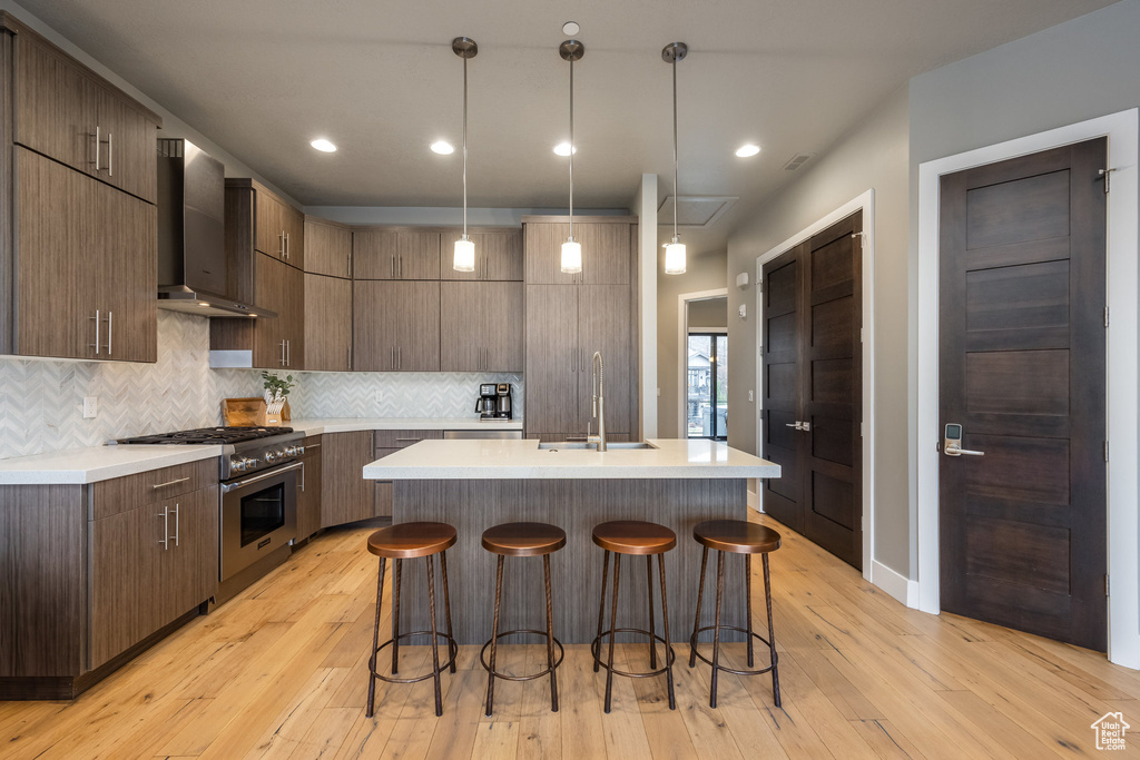 Kitchen with wall chimney range hood, light countertops, a kitchen bar, high end stainless steel range, and modern cabinets