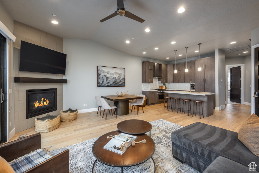 Living area with light wood-style floors, vaulted ceiling, a fireplace, baseboards, and a ceiling fan