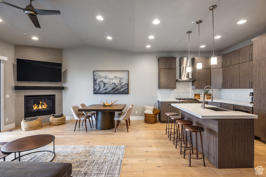 Kitchen featuring a kitchen breakfast bar, a sink, light countertops, open floor plan, and wall chimney exhaust hood