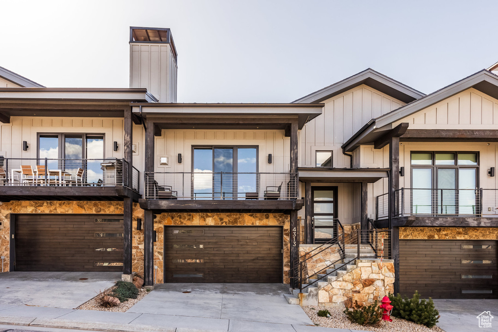 View of front facade with concrete driveway, an attached garage, board and batten siding, and a balcony