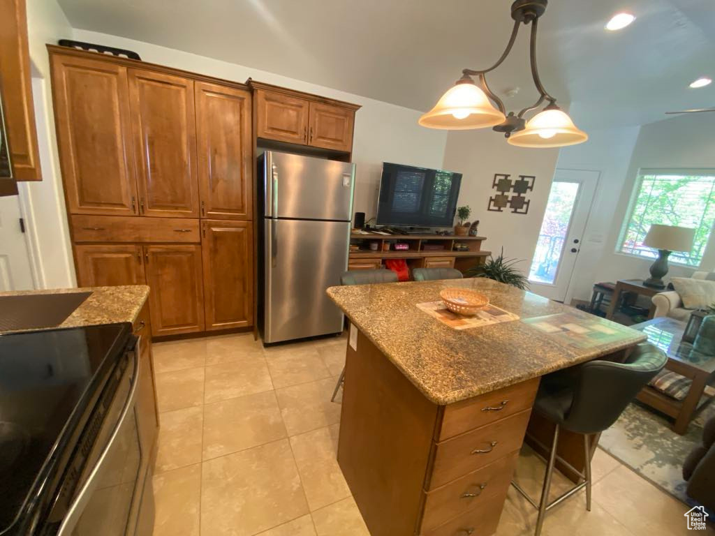 Kitchen featuring light stone counters, a breakfast bar area, stainless steel appliances, a center island, and brown cabinetry