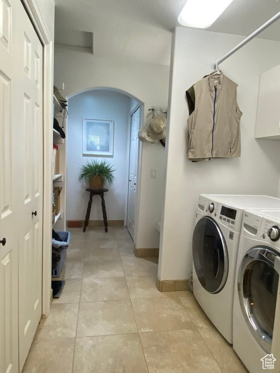 Washroom with light tile patterned floors, washer and dryer, arched walkways, and baseboards