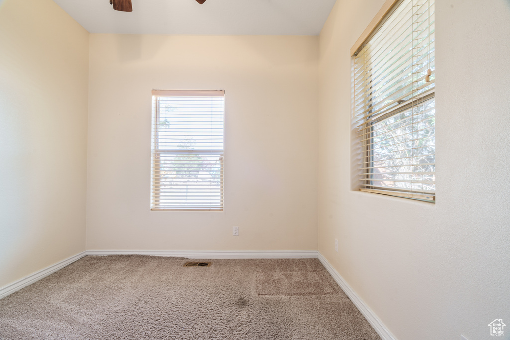 Carpeted empty room featuring a ceiling fan, visible vents, and baseboards