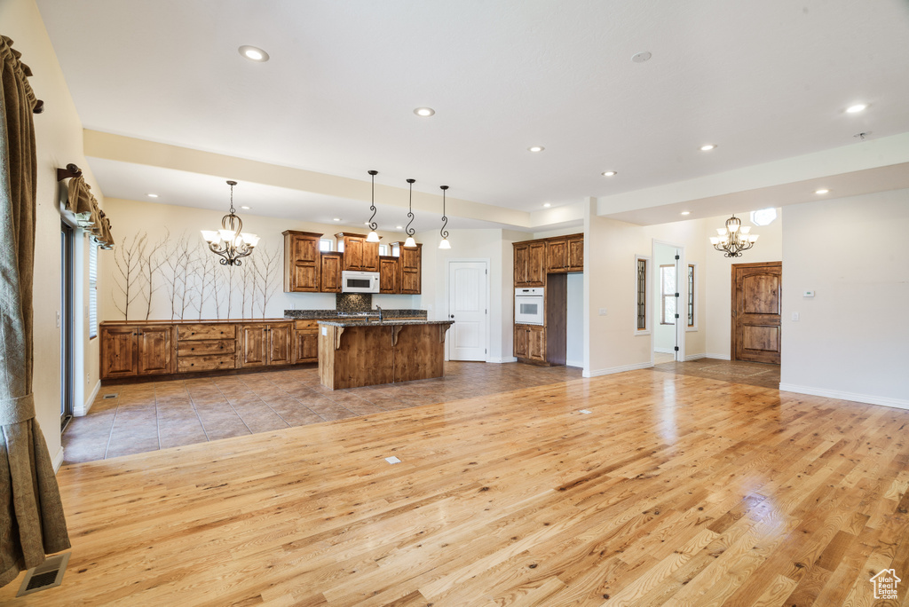 Kitchen featuring recessed lighting, an inviting chandelier, brown cabinets, light wood-type flooring, and white appliances