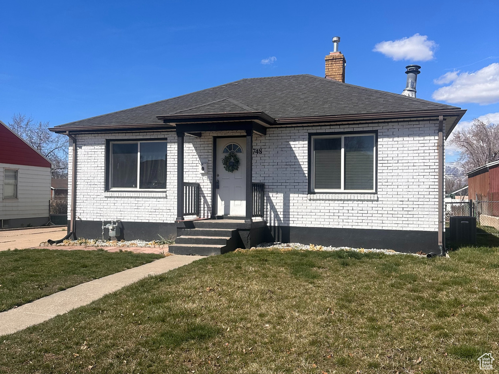 View of front of home with a front yard, a chimney, central AC unit, and brick siding