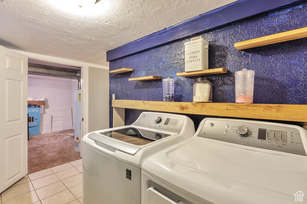 Clothes washing area with a textured ceiling, light tile patterned floors, water heater, separate washer and dryer, and laundry area