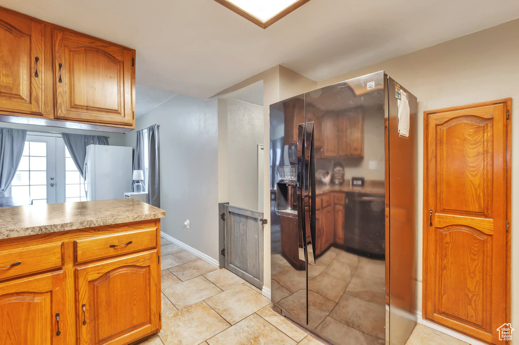 Kitchen with black refrigerator with ice dispenser, brown cabinets, light countertops, and baseboards
