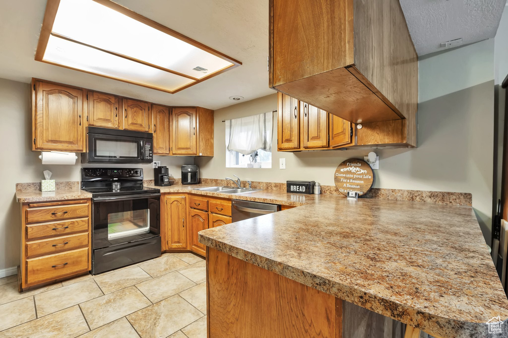 Kitchen featuring brown cabinets, a sink, light countertops, black appliances, and light tile patterned flooring