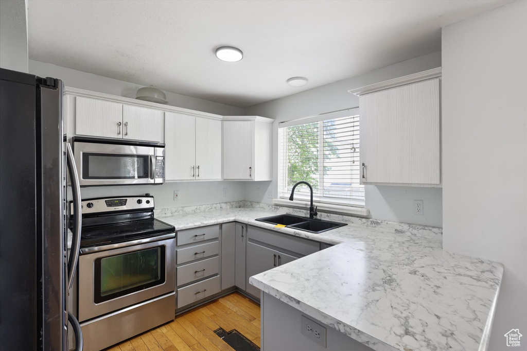 Kitchen featuring a sink, gray cabinets, a peninsula, light countertops, and appliances with stainless steel finishes