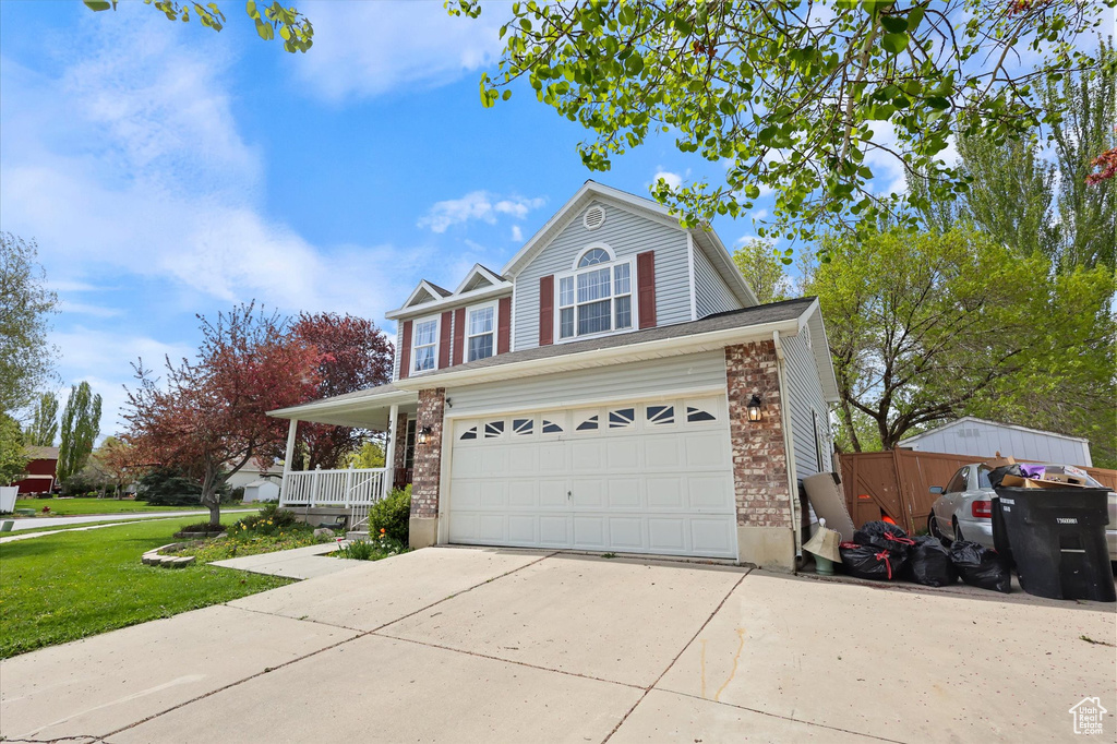 Traditional-style house with a front lawn, covered porch, brick siding, concrete driveway, and an attached garage