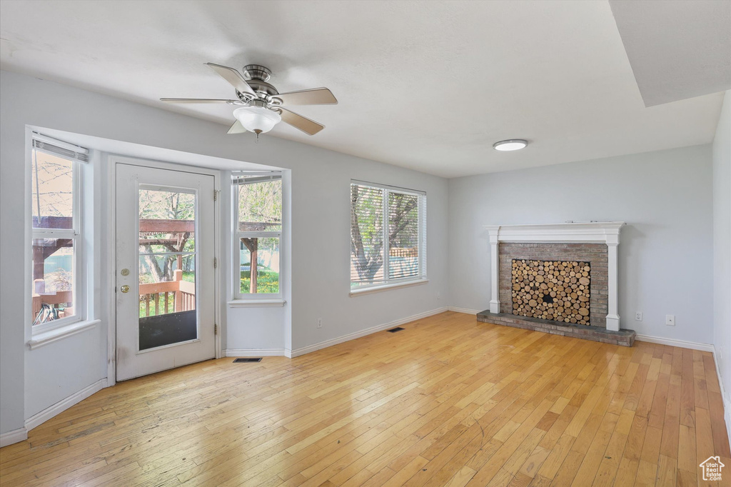 Unfurnished living room with baseboards, ceiling fan, light wood-style flooring, and a brick fireplace