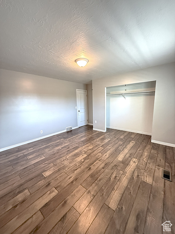 Unfurnished bedroom featuring dark wood-style floors, a textured ceiling, and a closet