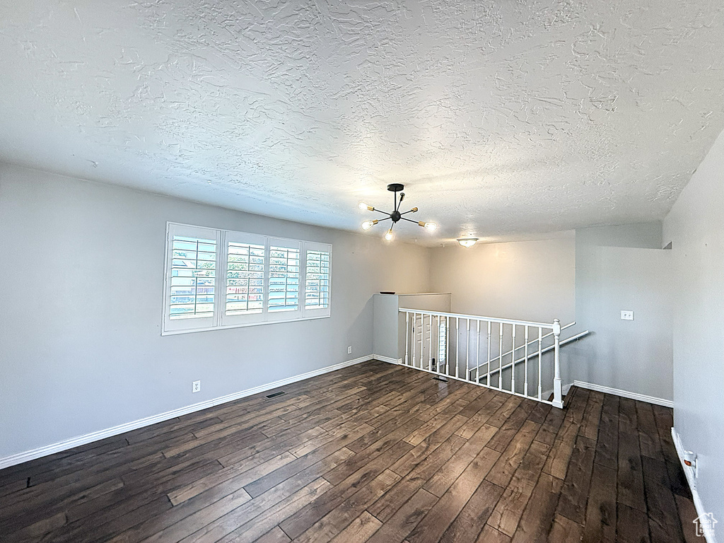 Unfurnished room with a chandelier, dark wood finished floors, and a textured ceiling
