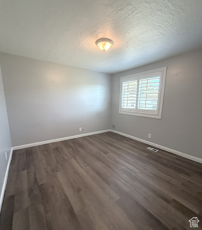 Empty room with dark wood-type flooring and a textured ceiling