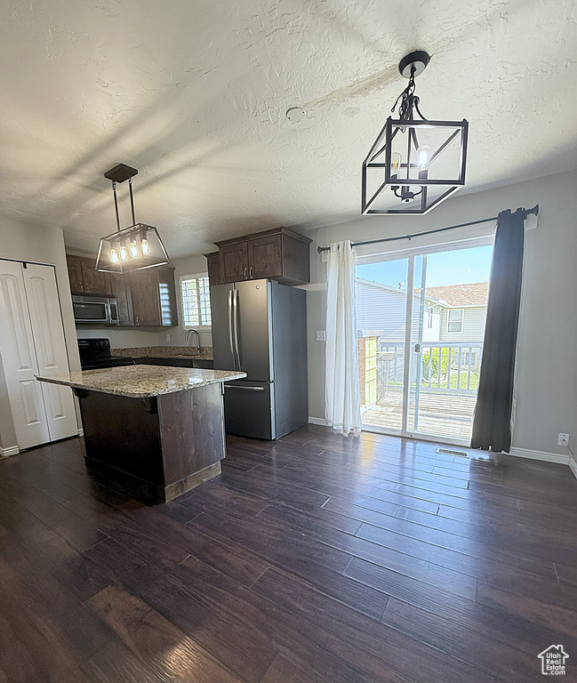 Kitchen with appliances with stainless steel finishes, a chandelier, dark brown cabinetry, dark wood-style flooring, and a textured ceiling