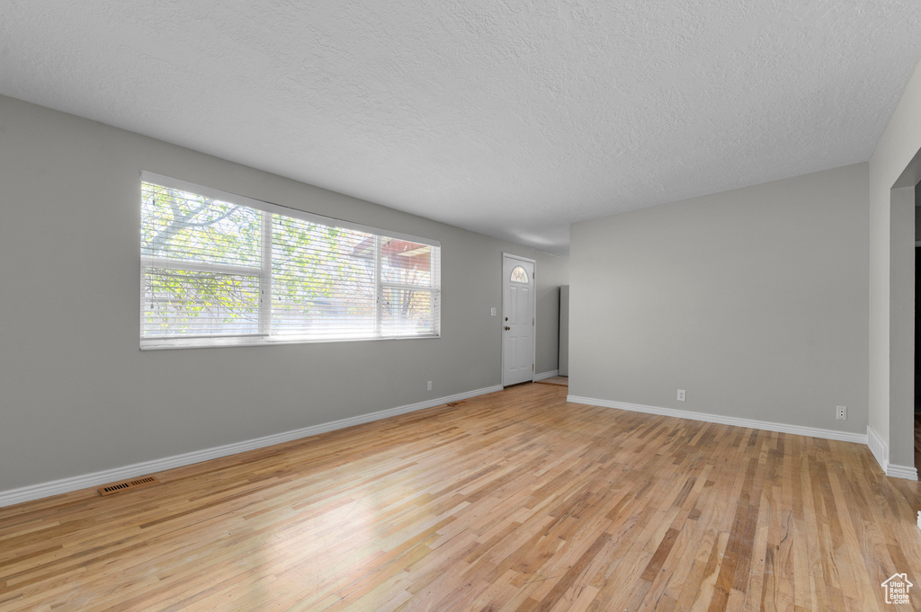 Unfurnished living room featuring a textured ceiling, visible vents, light wood-style flooring, and baseboards