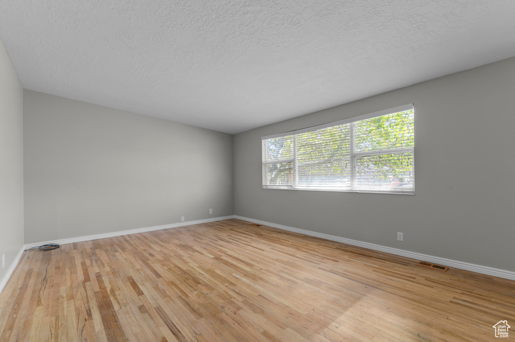 Unfurnished room with a textured ceiling, visible vents, light wood-type flooring, and baseboards