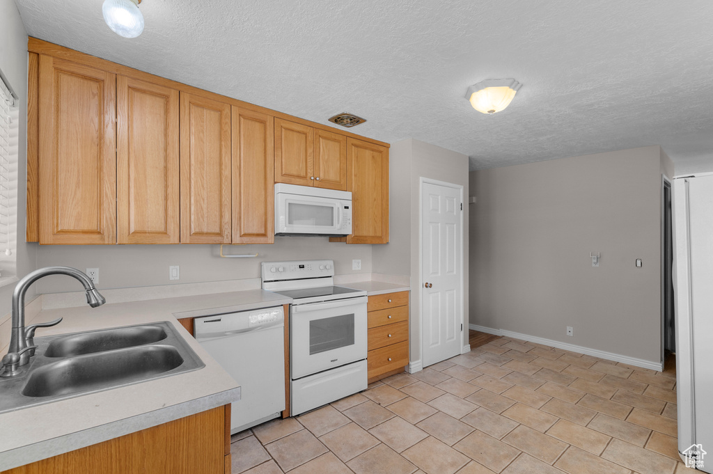 Kitchen featuring white appliances, light countertops, a sink, baseboards, and a textured ceiling
