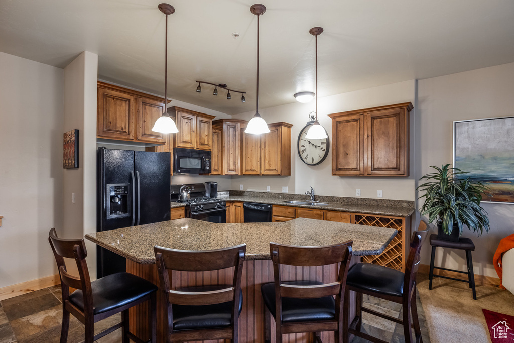 Kitchen with pendant lighting, brown cabinets, a sink, baseboards, and black appliances