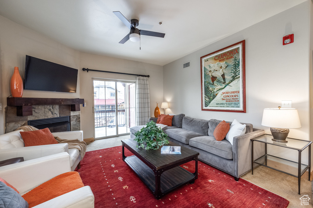 Living room featuring a stone fireplace, visible vents, ceiling fan, and carpet