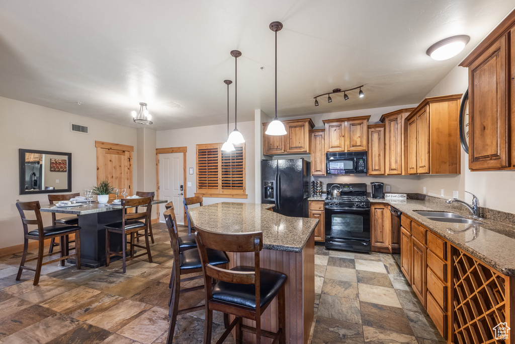 Kitchen featuring a sink, brown cabinetry, a center island, black appliances, and stone finish floor